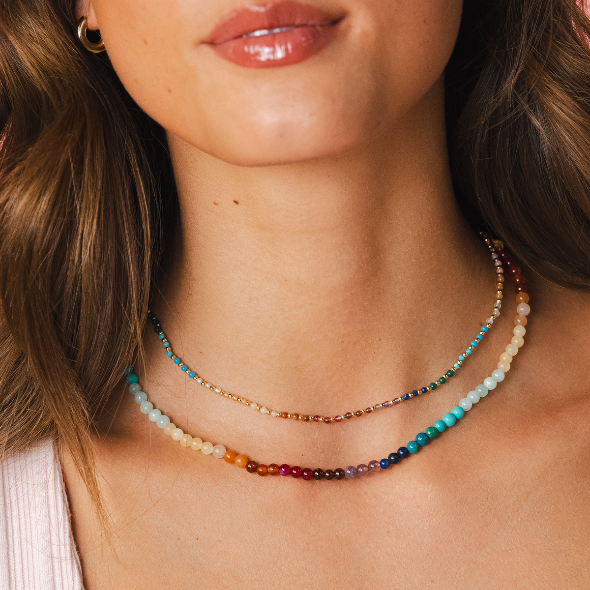 Model wearing a healing necklace stack. The necklaces include a 2mm multicolor stone and gold bead healing necklace and a 4mm multicolor stone healing necklace