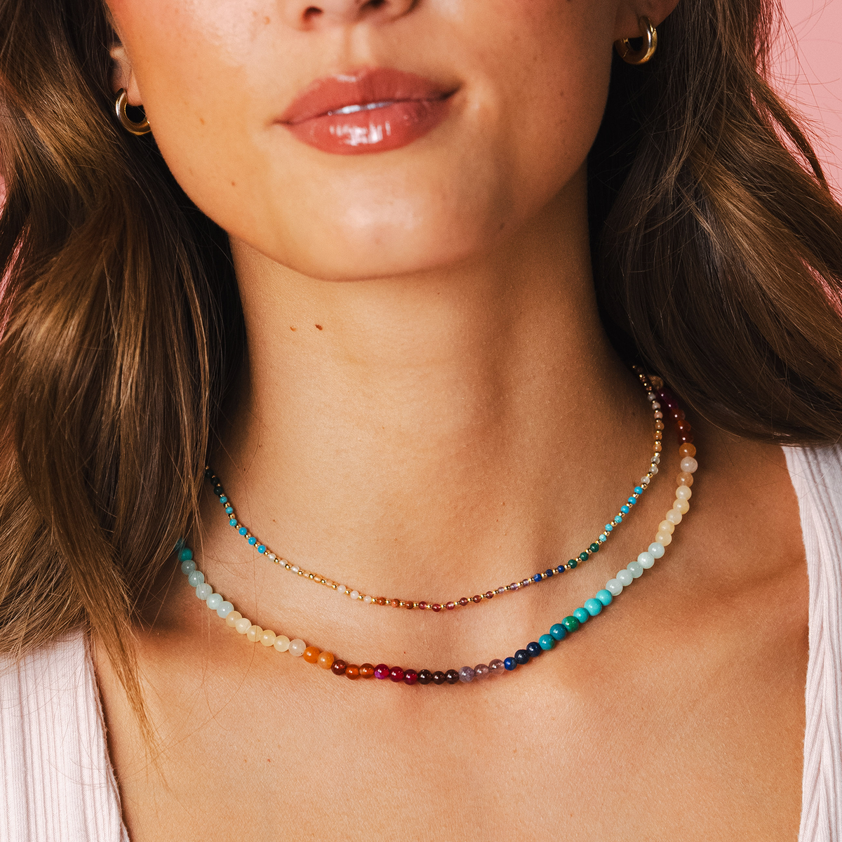 Model wearing a necklace stack. The necklaces include a 4mm multicolor stone healing necklace and a 2mm multicolor stone and gold bead healing necklace