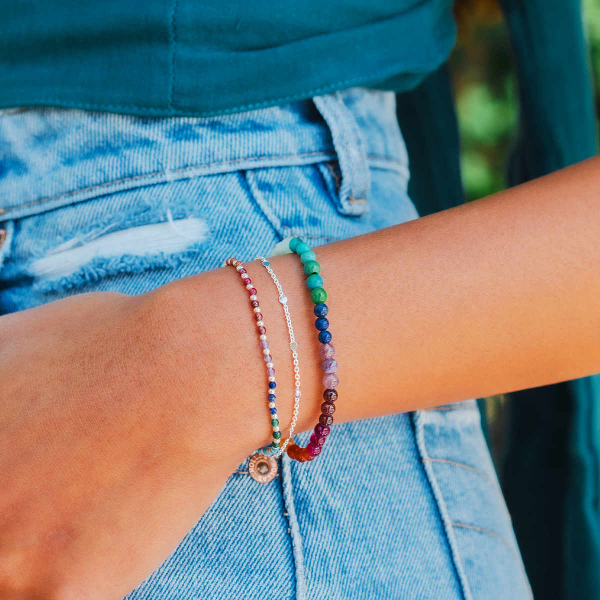 Model wearing a stack of three bracelets. The bracelets include a dainty silver chain bracelet, a 4mm multicolor stone healing bracelet, and a 2mm multicolor stone and gold bead healing bracelet 