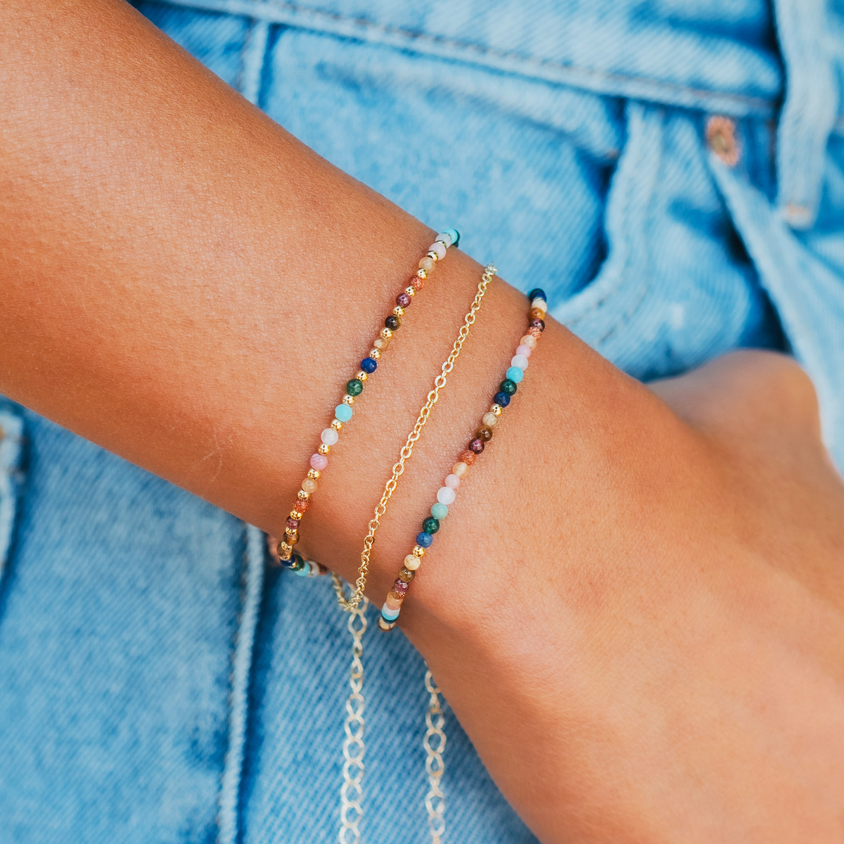 Model wearing a healing bracelet stack. The bracelets consist of a 2mm multicolor stone and gold bead healing bracelet and a 2mm multicolor stone healing bracelet.