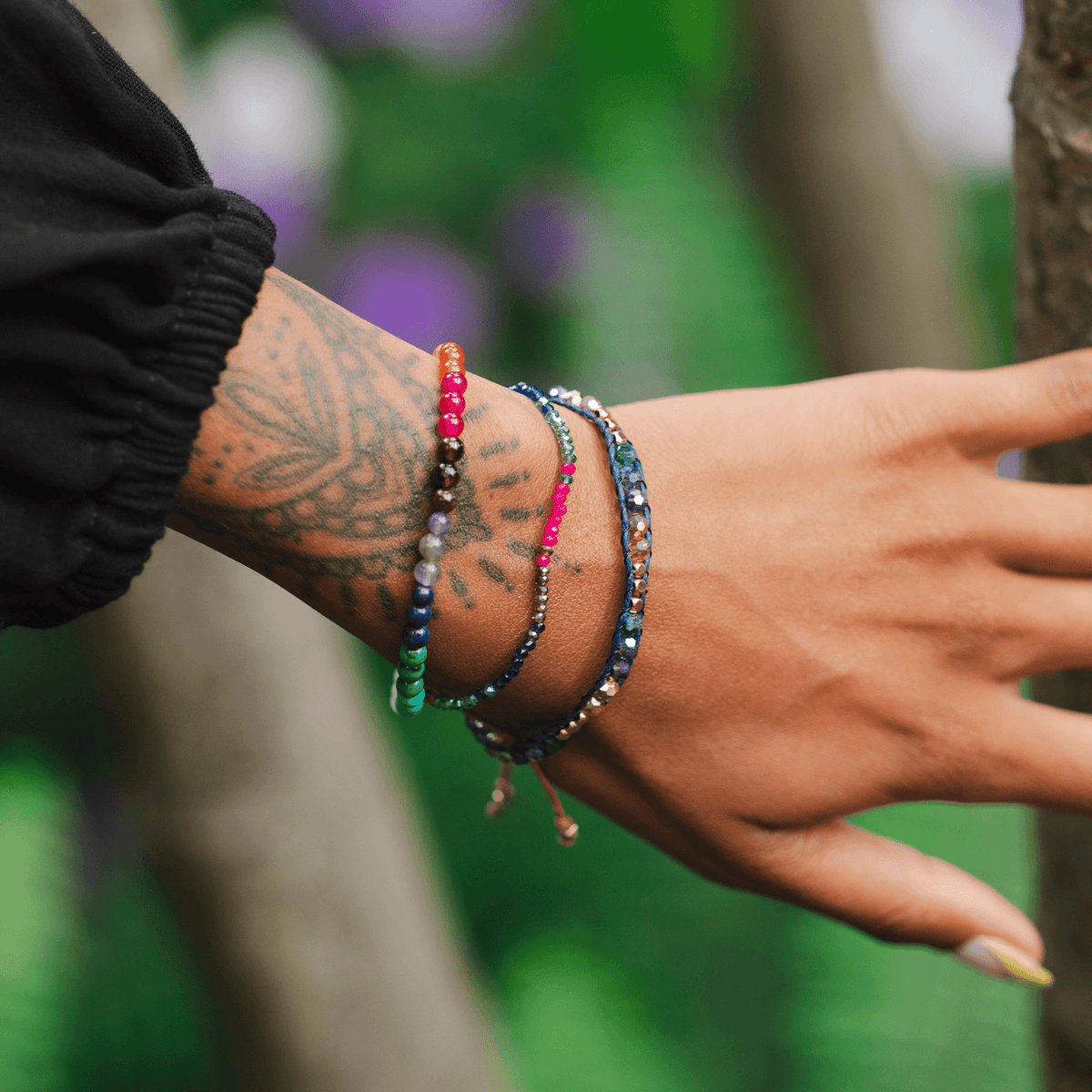 Model wearing a stack of bracelets. The bracelets include a pink, green and blue stone goddess bracelet, a 4mm multicolor stone healing bracelet and a purple, blue and orange stone single wrap bracelet