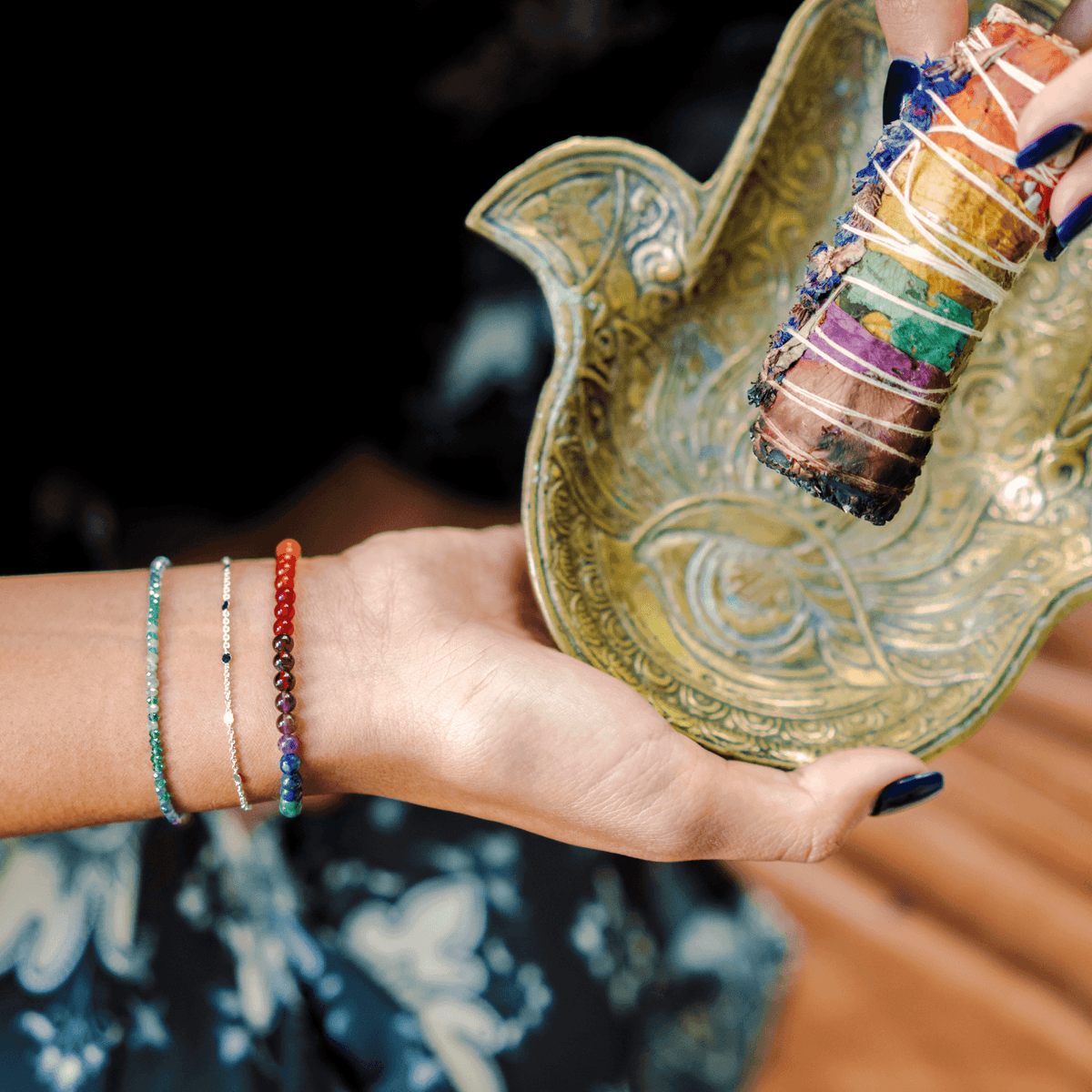 Model holding a sage smudge stick while wearing a 4mm multicolor stone healing bracelet, a dainty silver chain bracelet and a green and blue stone goddess bracelet