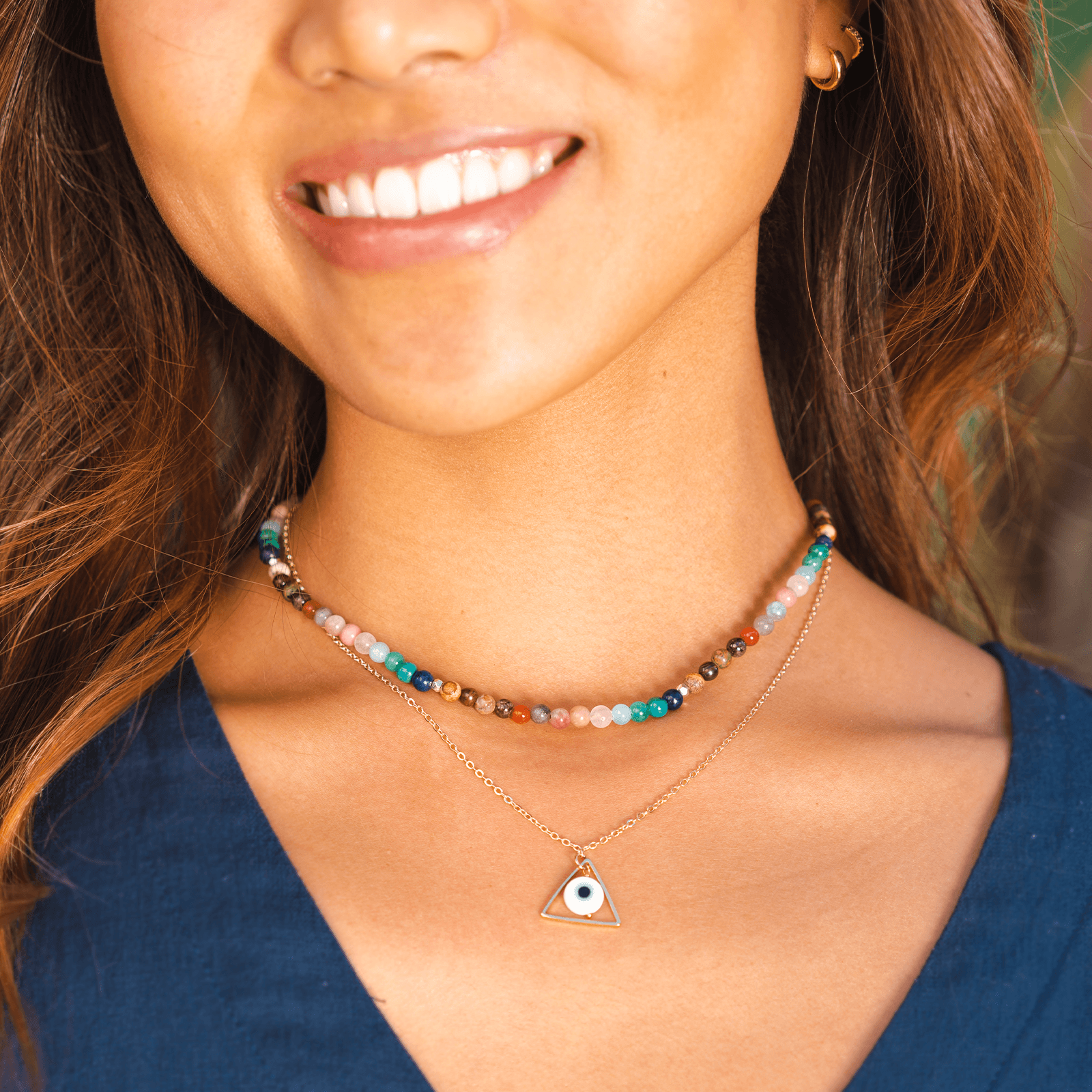 Model wearing a stack of two necklaces. The necklaces include a 4mm multicolor stone healing necklace and a evil eye necklace on a gold chain