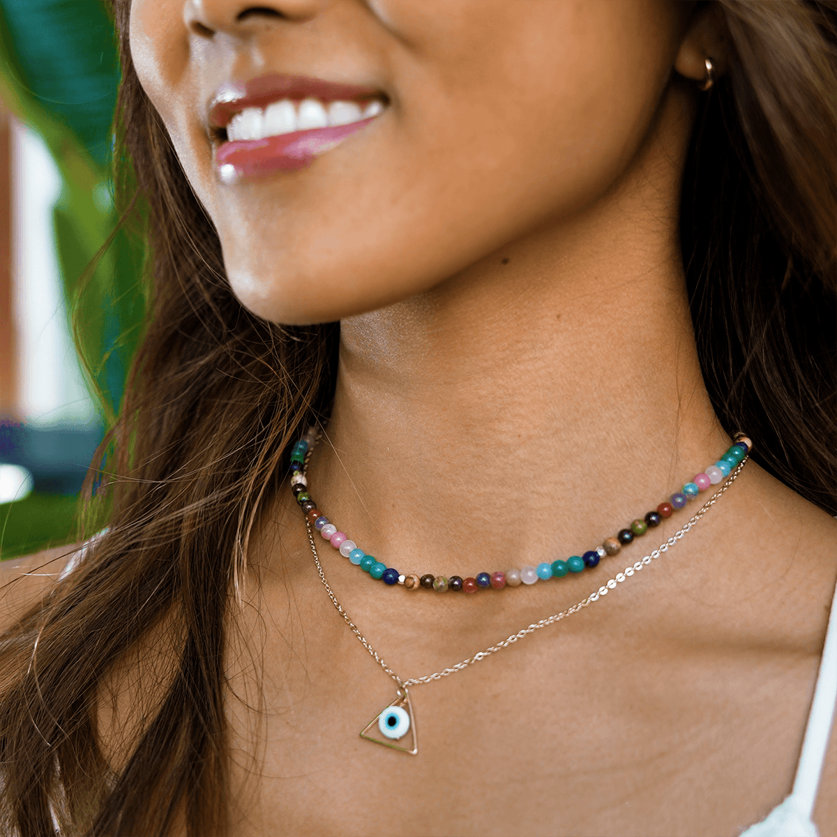 Model wearing a stack of two necklaces. The necklaces include a 4mm multicolor stone healing necklace and a evil eye necklace on a gold chain