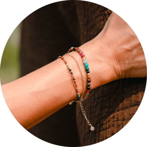 Model wearing a stack of three bracelets. Bracelets include a 4mm multicolor stone bracelet, a 2mm multicolor stone bracelet and a dainty gold chain bracelet