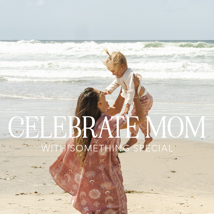 Woman is pink kimono and harem pant lounge set holding baby on the beach