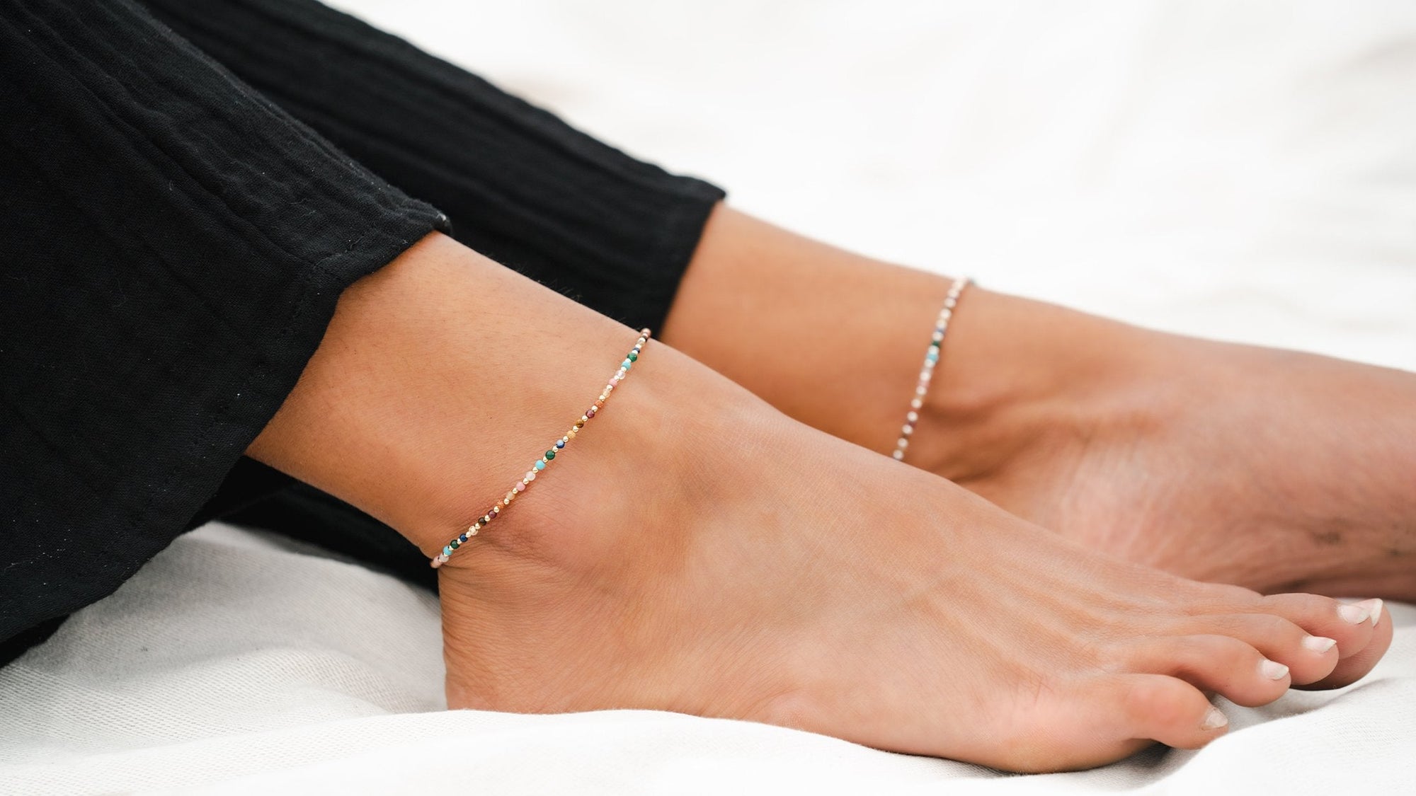 Woman wearing women's anklet on both feet. Dainty gold anklet on and a dainty silver anklet on the other food. Master Healer healing energy stone anklet.
