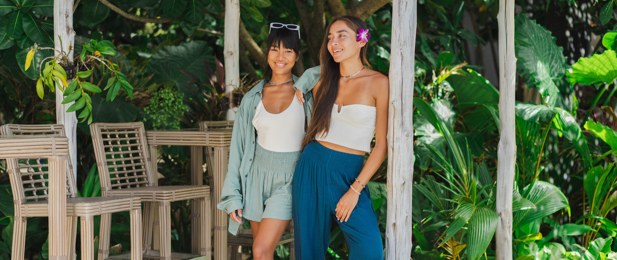 Two women standing nect to each other, one wearing a sage crinkle gauze cotton button up and sage shorts and the other wearing flowy beach pants in blue.