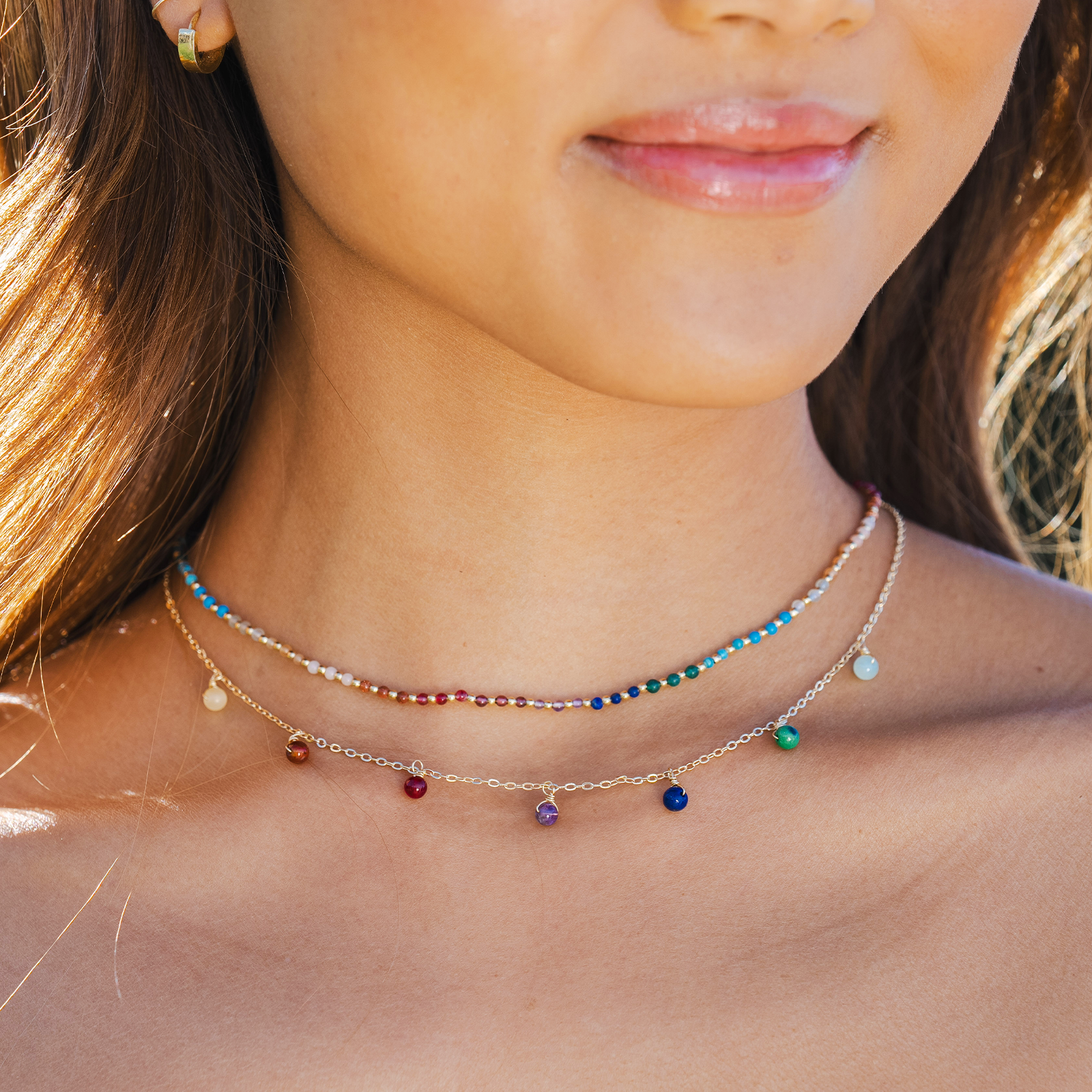 Model wearing a necklace stack. The necklaces include a multicolor stone dewdrop charm healing necklace with a gold chain and a 2mm multicolor stone and gold bead healing necklace