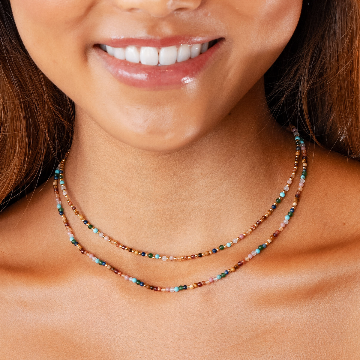 Model wearing a healing necklace stack. The necklaces include a 2mm multicolor stone and gold bead healing necklace and a 2mm multicolor stone healing necklace