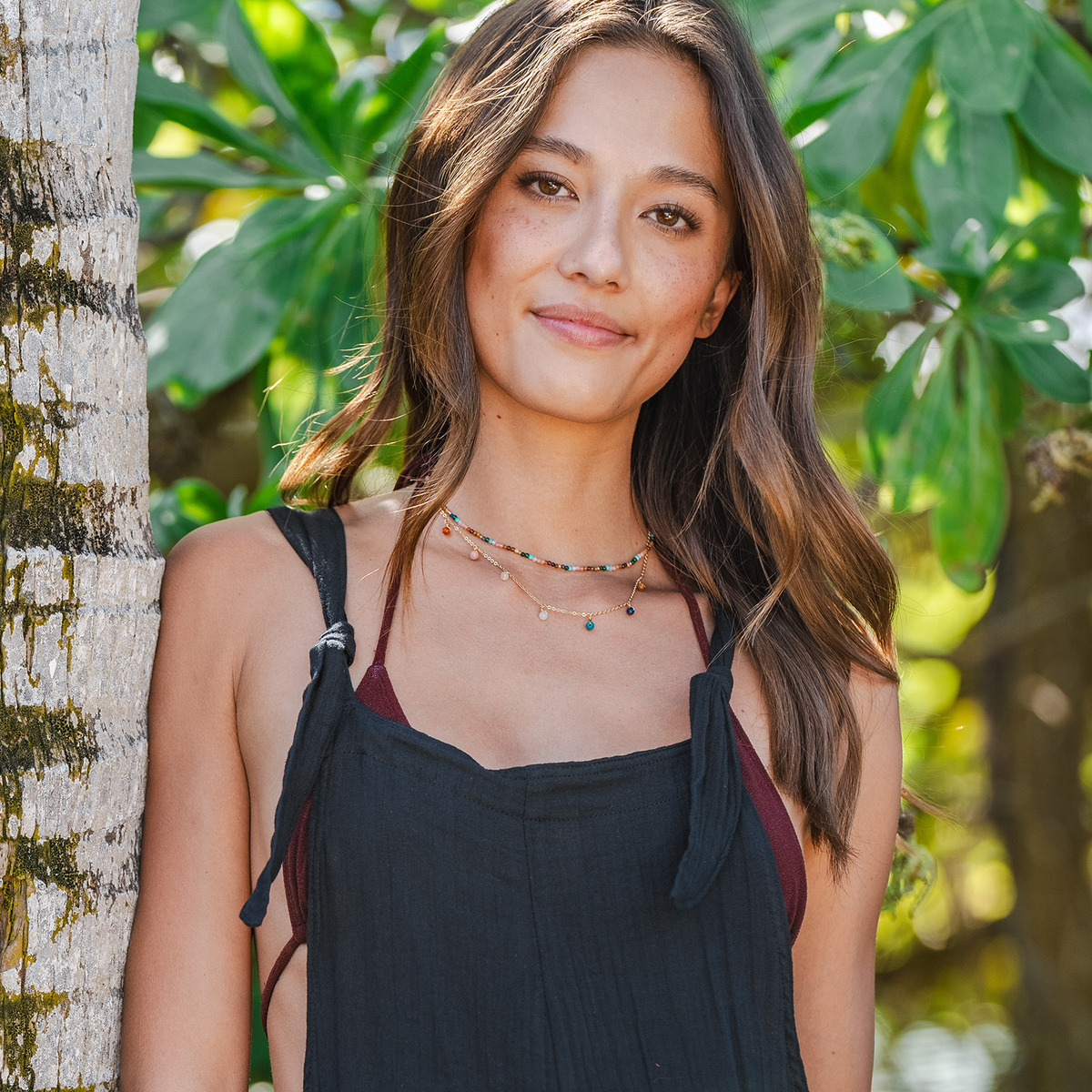 Model wearing a healing necklace stack. The stack includes a 2mm multicolor stone healing necklace and a gold chain necklace with multicolor stone dewdrop charms