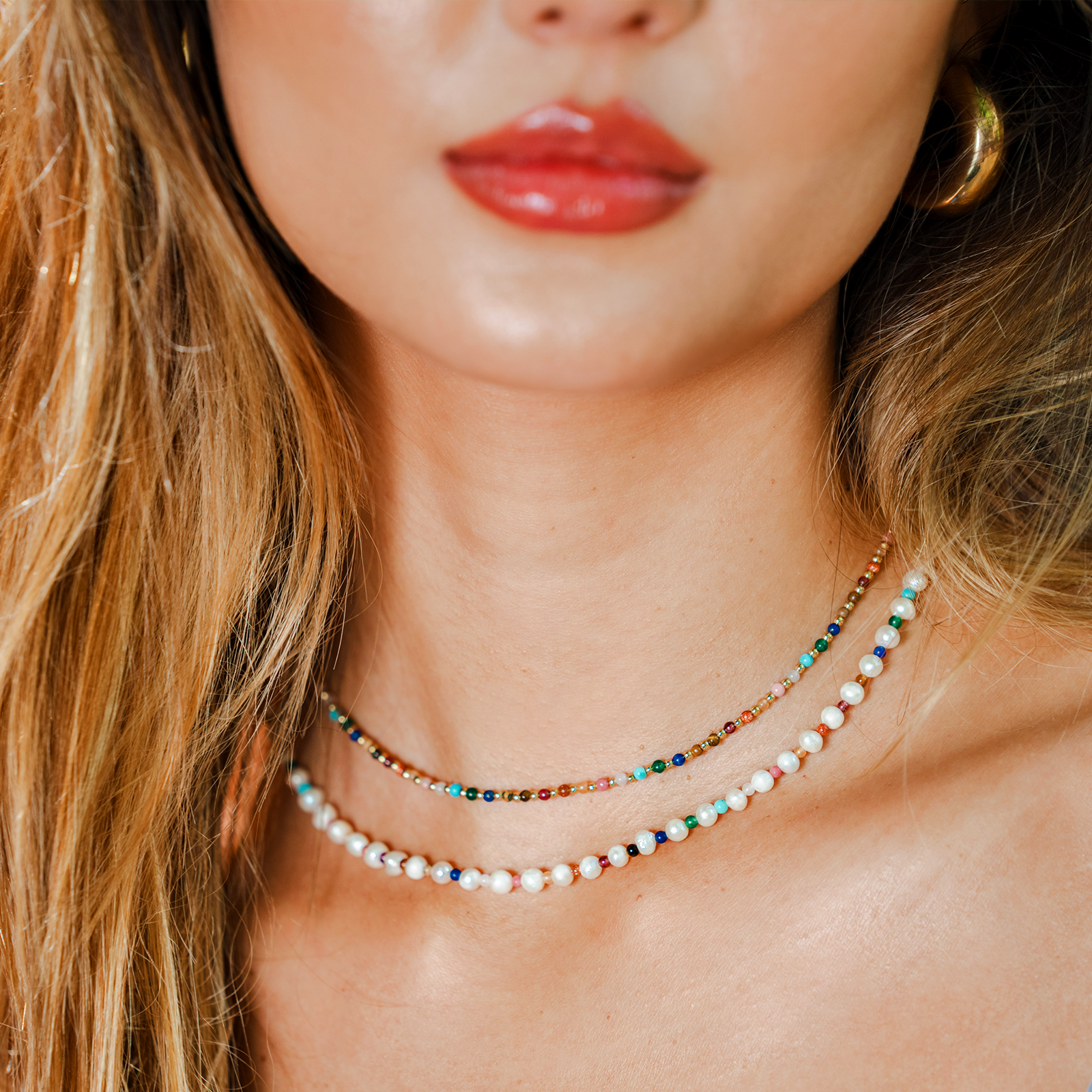 Model wearing a stack of two healing necklaces. The necklaces include a pearl and 2mm multicolor stone healing necklace and a 2mm multicolor stone and gold bead healing necklace