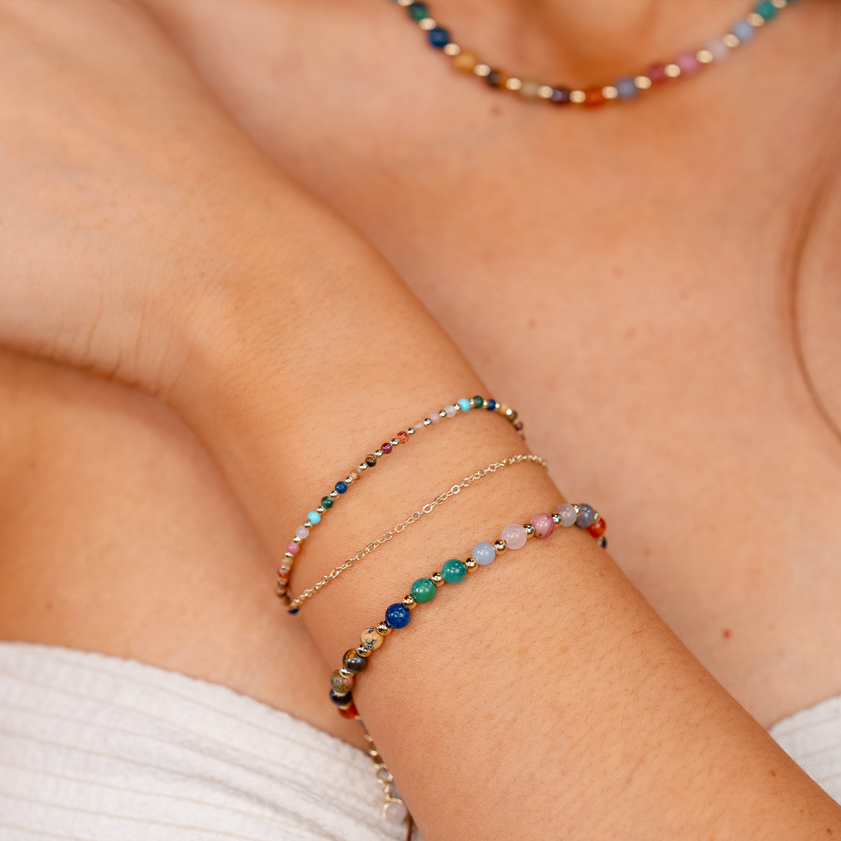 Model wearing a stack of two healing bracelets. The bracelets include a 4mm multicolor stone and gold bead healing bracelet and a 2mm multicolor stone and gold bead healing bracelet