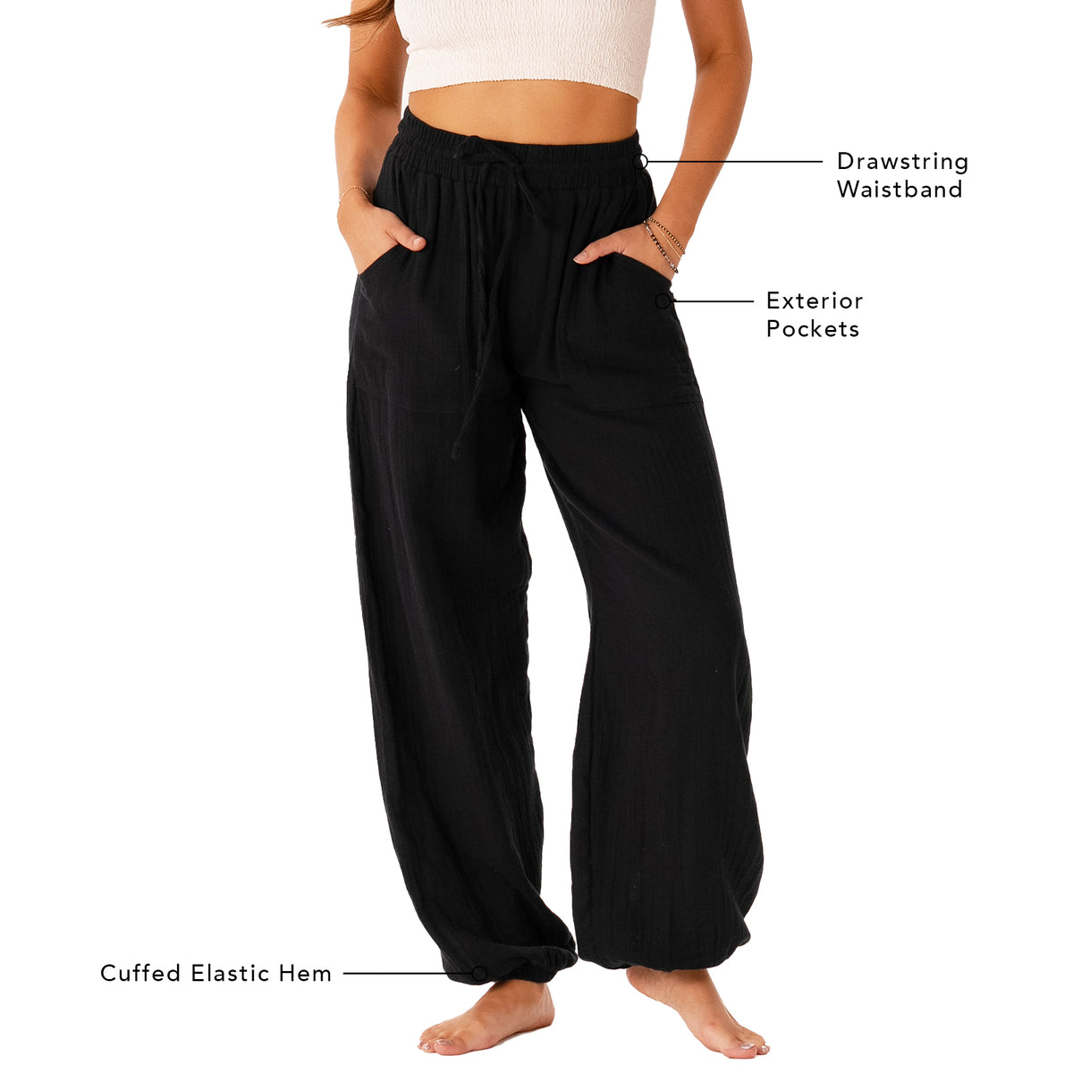 Model wearing black harem pants with a drawstring waistband. The picture outlines different features of the pants including a drawstring waistband, exterior pockets and a cuffed elastic hem