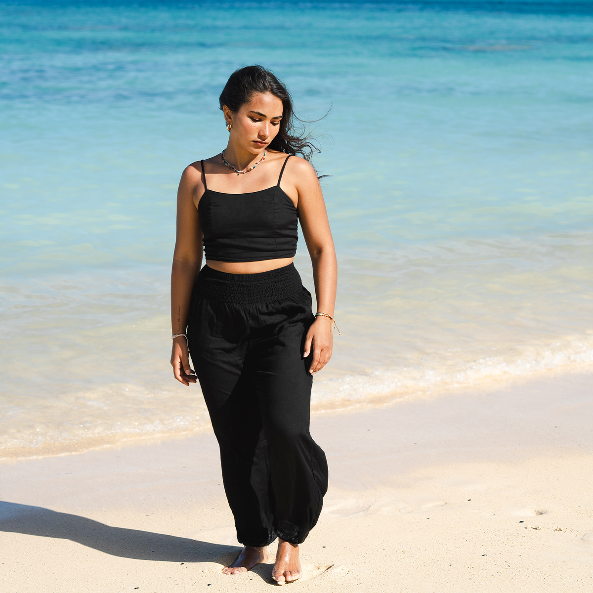 Model standing on the beach wearing black harem pants and a black rayon tank top