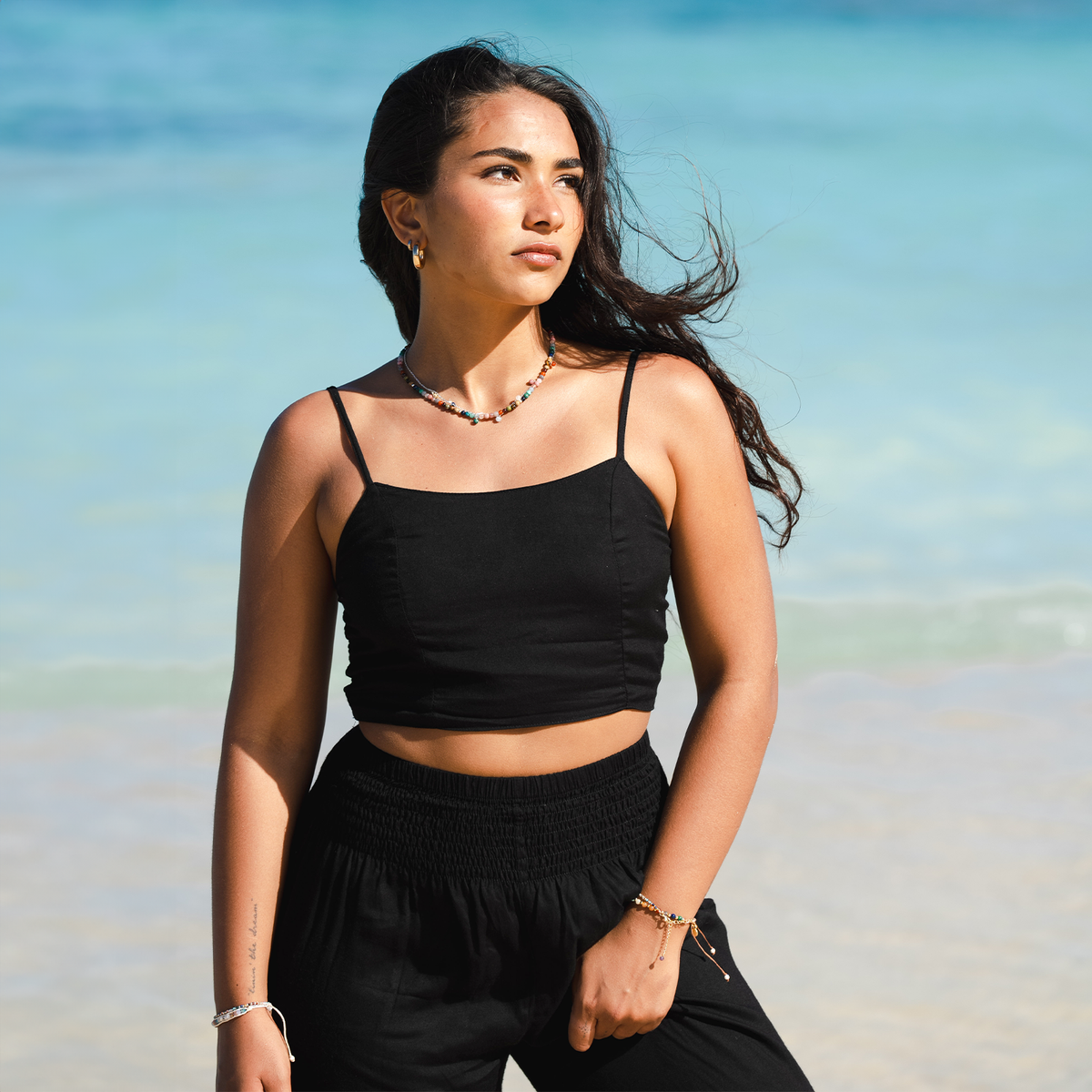 Model standing in front of the ocean wearing black harem pants and a black rayon tank top