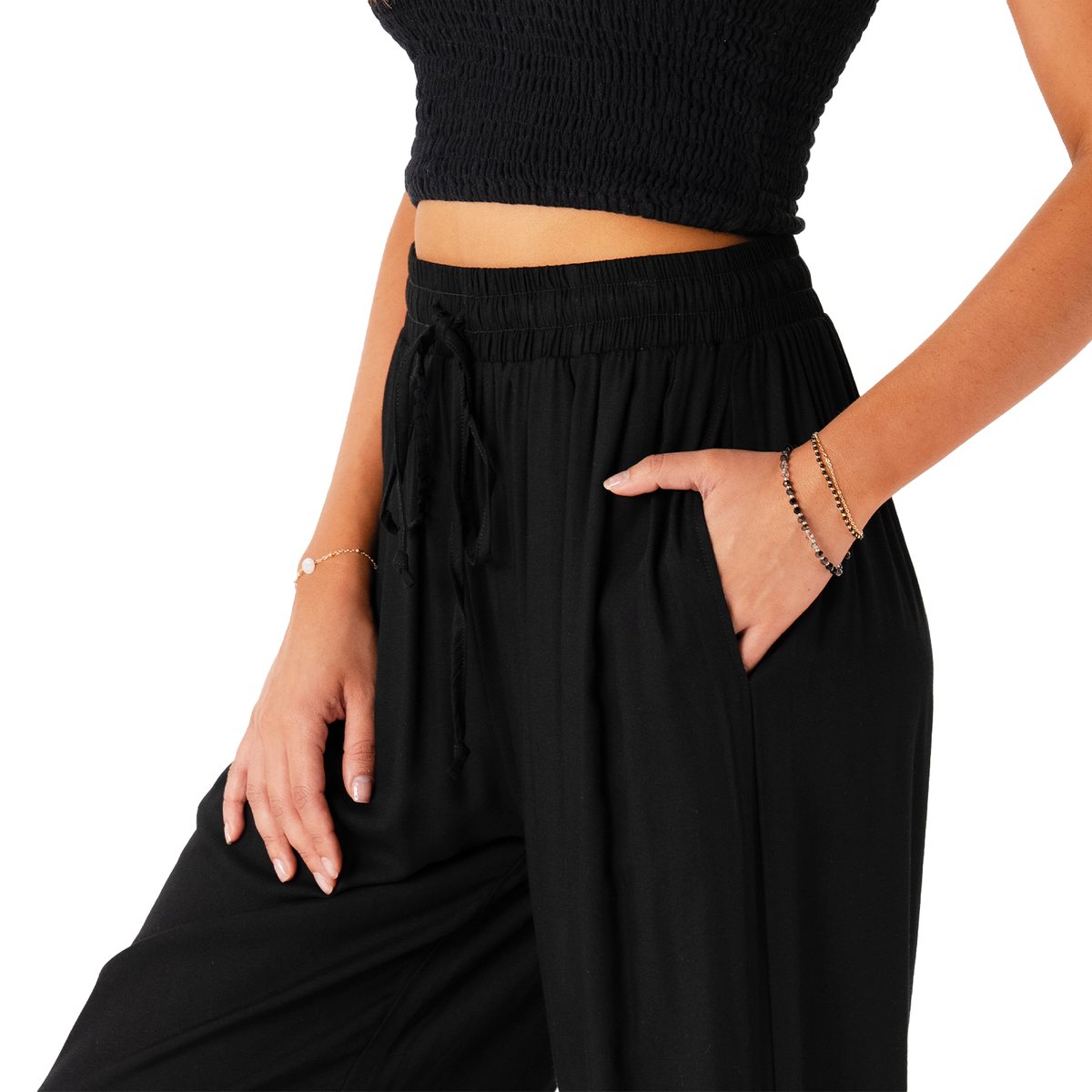 A close up photo of a model wearing black harem pants with a drawstring waistband