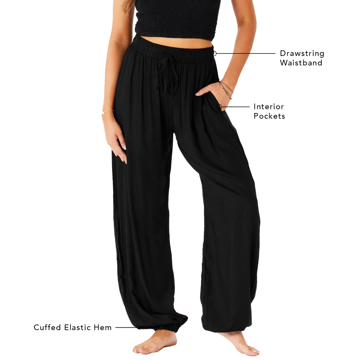 Model wearing black harem pants with a drawstring waistband. The photo outlines the features of the pants including a drawstring waistband, interior pockets, and a cuffed elastic bottom hem