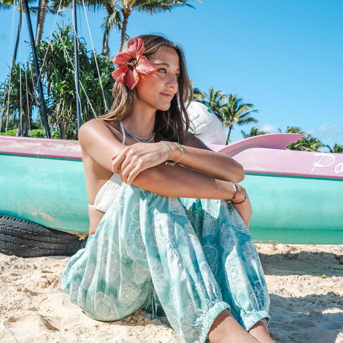 Model sitting on the beach in Hawaii wearing light teal and white mandala paisley print harem pants with a drawstring waistband