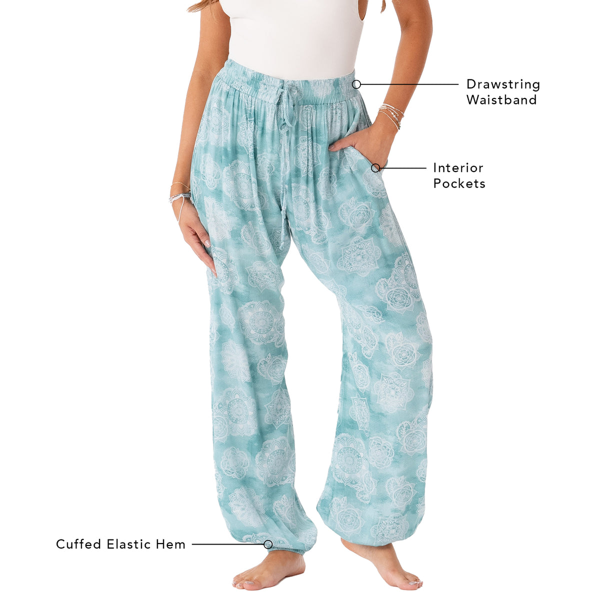 Model wearing light teal and white mandala paisley print harem pants with a drawstring waistband. The picture outlines the features of these pants including a drawstring waistband, interior pockets and a cuffed elastic bottom hem