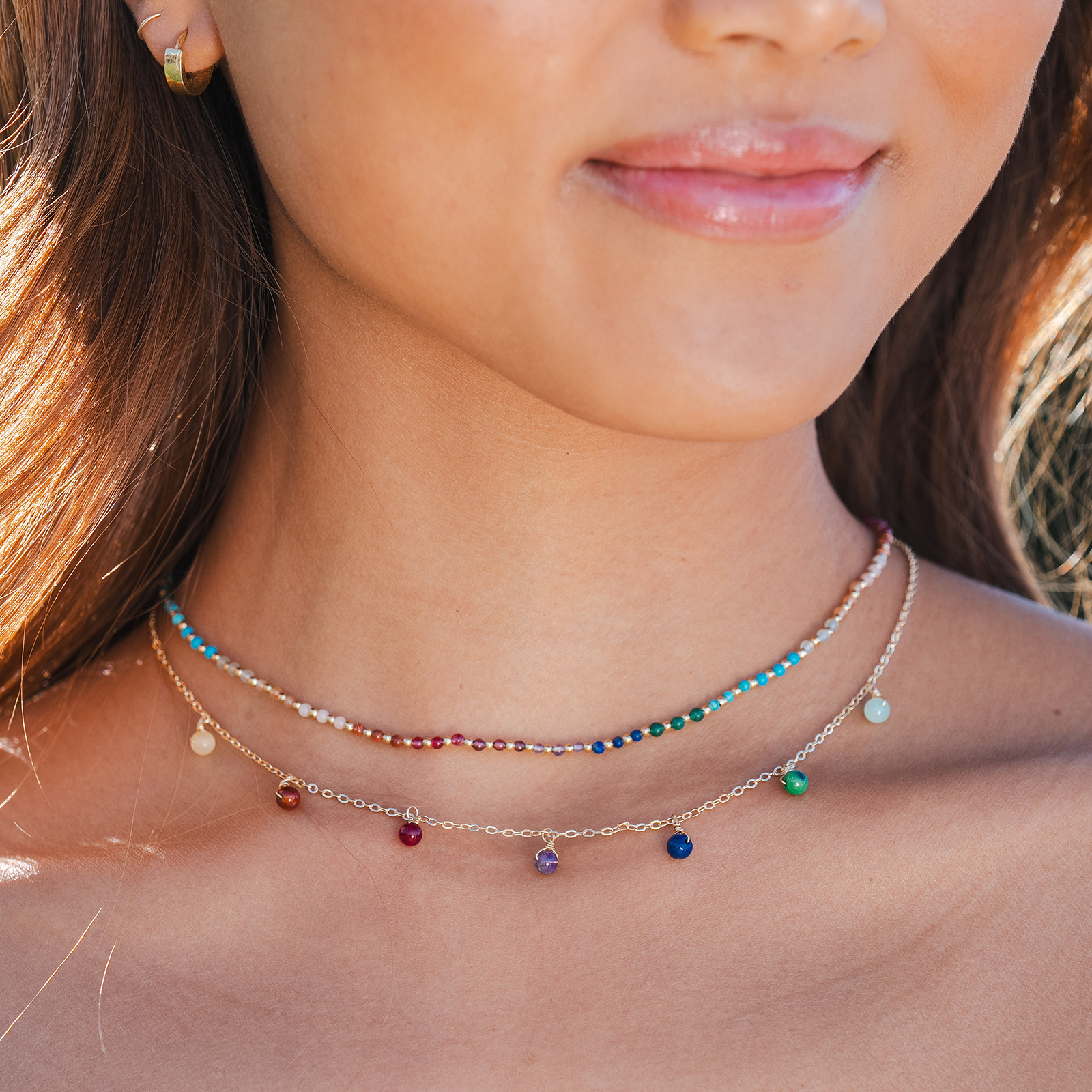 Model wearing a healing necklace stack. The necklaces include a 2mm multicolor stone and gold bead healing necklace and a multicolor stone dewdrop charm gold chain necklace