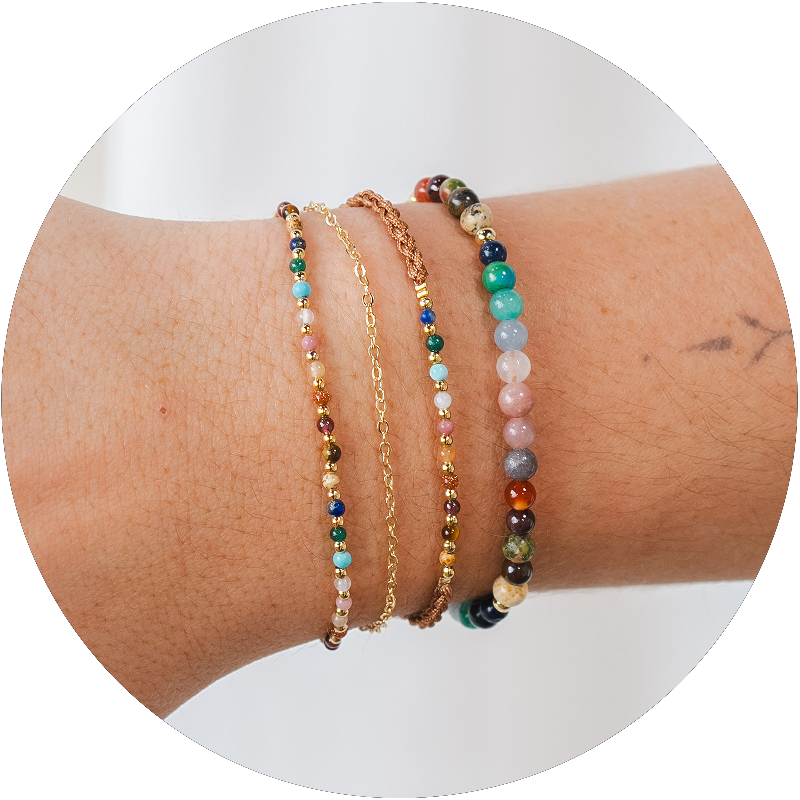 Model wearing a healing bracelet stack. The bracelets include a 2mm multicolor stone and gold bead bracelet with an attached gold chain bracelet, a 2mm multicolor stone and gold bead bracelet on a brown cotton braided cord and a 4mm multicolor stone healing bracelet
