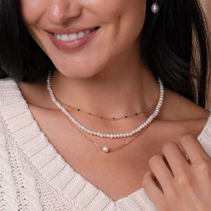 Pearl strand and gold chain necklaces, layered on neck