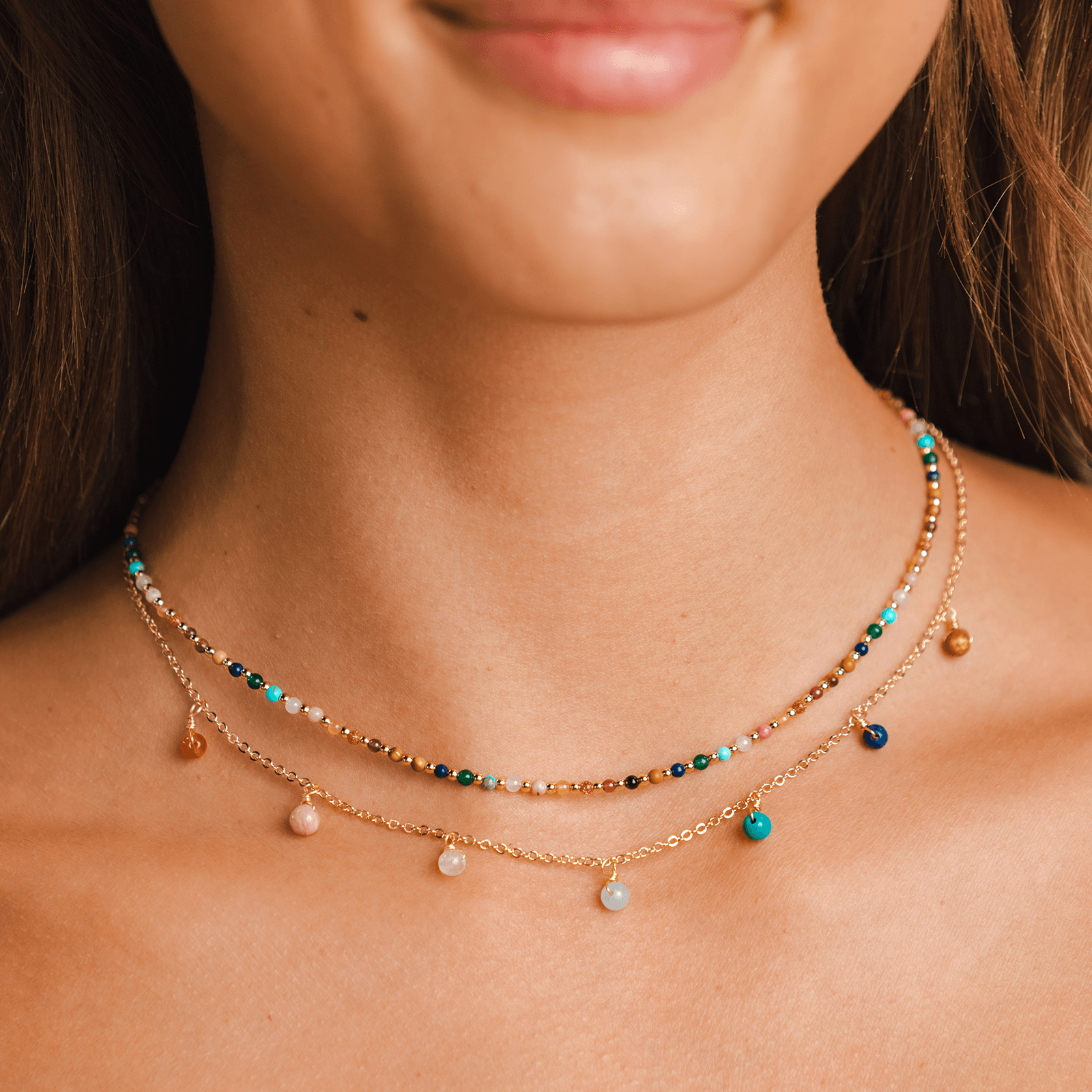 Necklace stack consisting of a gold chain necklace with assortment of rainbow bead dewdrop charms and a 2mm assorted rainbow stone and gold bead necklace