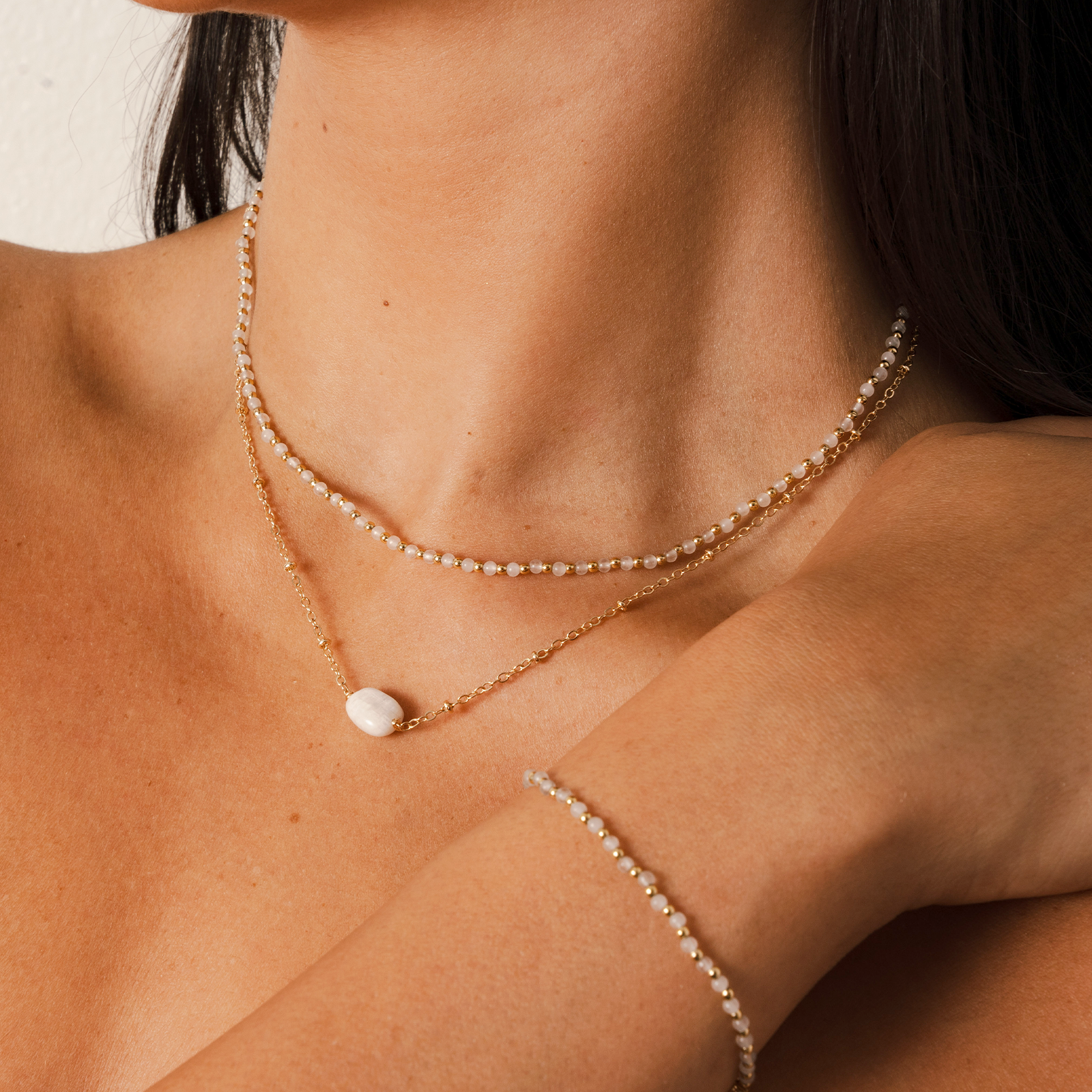 Model wearing a necklace stack. The stack consists of a 2mm moonstone and gold bead healing necklace and a moonstone healing necklace with a gold chain
