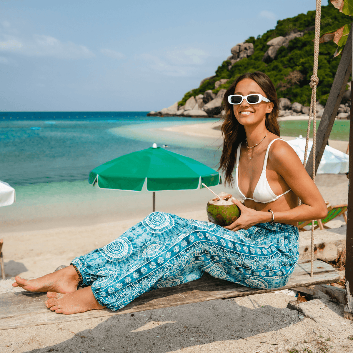 Model sitting on the beach wearing teal watercolor mandala print harem pants