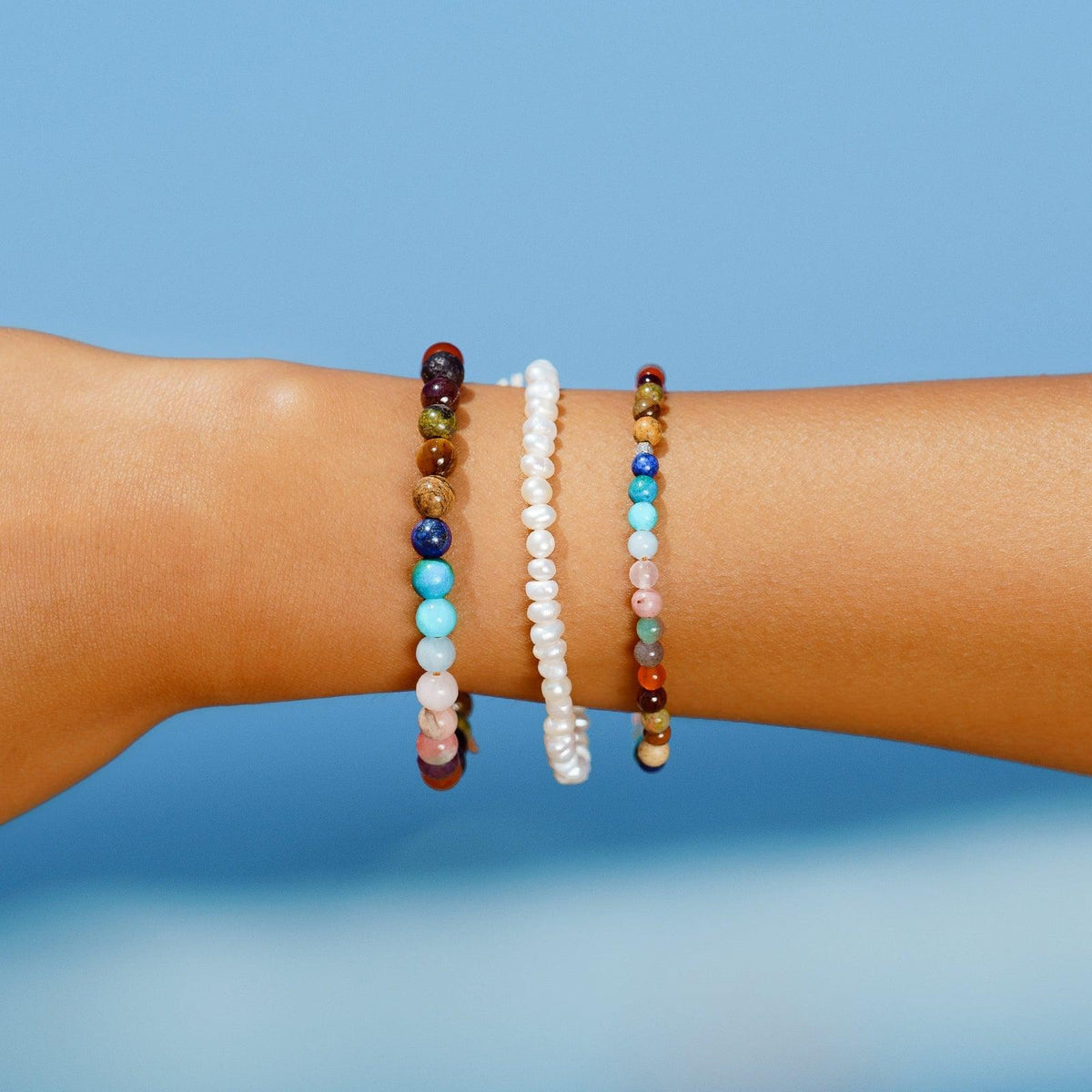 Model wearing a stack of three bracelets. The bracelets are a 4mm pearl bracelet, a 6mm multicolor stone bracelet and a 4mm multicolor stone bracelet