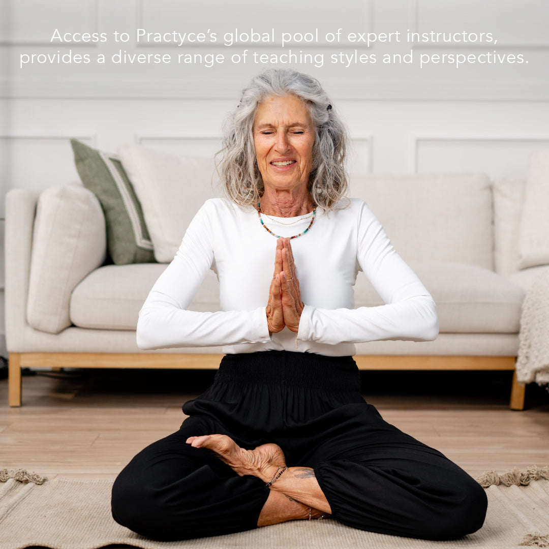 older model doing yoga in a living room with a long sleeve white top and black harem pants